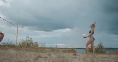 Spor bikinili güzel bayanlar yaz tatilinde plaj voleybolu oynuyorlar, atletik kadınlar zıplıyorlar.