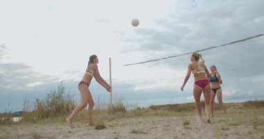 İki bayan plaj voleybol takımının dostça maçı, bayanlar yaz günü sahada bulutlu gökyüzüne karşı oynuyorlar.
