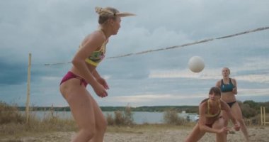 Spor bikinili dört kadın yaz günü kumlu sahada voleybol oynuyorlar. Spor ve aktif yaşam tarzları.