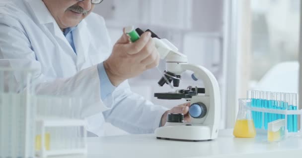 髭を生やした白人男性研究者は保護眼鏡をかけ、顕微鏡スパバで作業している。研究室で顕微鏡を使う科学者です。コロナウイルスワクチンの検索 — ストック動画