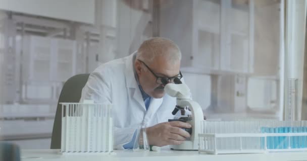 Investigador masculino caucásico barbudo que usa gafas protectoras y trabaja con un microscopio spbas. científico usando microscopio en un laboratorio. Búsqueda de vacuna contra el coronavirus — Vídeos de Stock