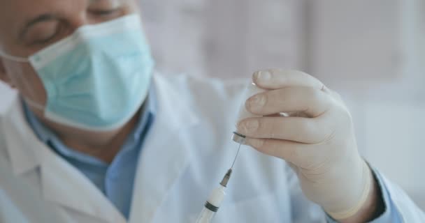 Læge hånd holder en sprøjte og en blå vaccine flaske på hospitalet. Sundhed og medicinske begreber. læge trækker vaccine til sprøjte, hætteglas, covid-19, coronavirus ampul, injektion – Stock-video