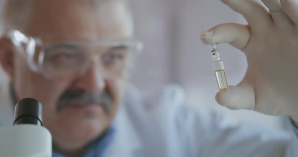 Imunização, tratamento Covid-19 Coronavirus. Retrato próximo de um médico masculino em óculos de proteção segurando um tubo de ensaio com a vacina de inscrição covid 19 sars-cov-2 em sua mão — Vídeo de Stock