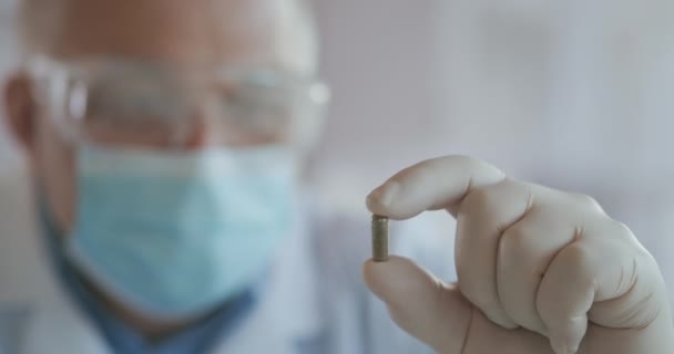 Extreme close-up van de wetenschapper in de masker ontwikkelaar van het vaccin tegen het coronavirus houdt de groene in zijn handen. De dokter kijkt naar de pijnstillers antivirale medicatie. Vitaminen — Stockvideo