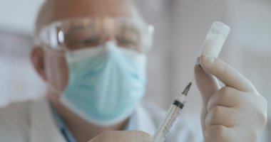 Doktor elinde bir şırınga ve mavi bir aşı şişesi tutuyor. Sağlık ve tıbbi kavramlar. Doktor şırıngaya, şişeye, kovid 19 'a, koronavirüs ampulüne, enjeksiyona aşı yapar.