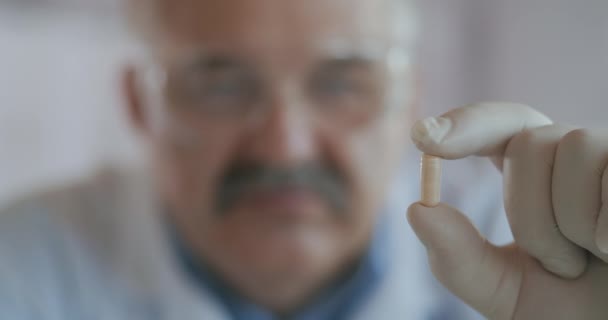 一位年长的男性科学家医生拿着一个白色胶囊，近距离观察它。病毒药物 — 图库视频影像
