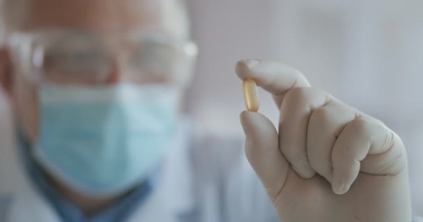 마스크를 쓴 과학자가 노란색 알약을 들고 있는 코로나 바이러스 백신을 개발하는 장면이 극적으로 근접 했습니다. 의사는 진통제 항바이러스제를 살펴 봅니다. 비타민 — 비디오