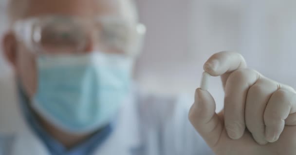 Extreme Close-up of a masked scientist developing a coronavirus vaccine holding a white pill. The doctor looks at the painkillers antiviral medication. Vitamins — Stock Video