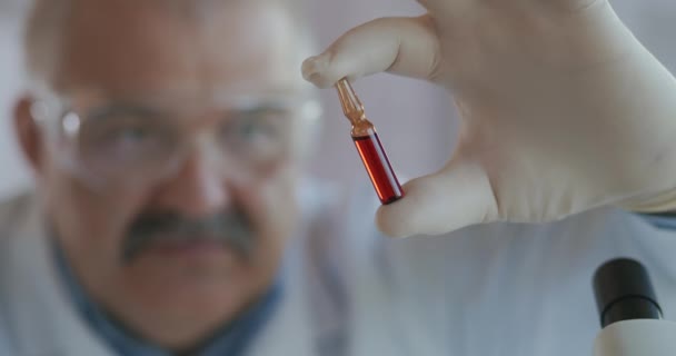 Immunizáció, kezelés Covid-19 Coronavirus. Szoros portré egy férfi orvosról védőszemüvegben, kezében egy kémcsővel, a felirat vakcina kovid 19 sars-cov-2 a kezében — Stock videók