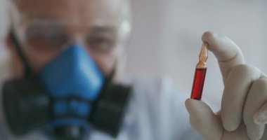 Mavi solunum cihazı ve koruyucu gözlüklü bir bilim adamının aşırı yakın çekimi, elinde kırmızı ampul tutan bir koronavirüs aşısı geliştiricisi. Doktor yeni aşıyı inceliyor. Yeni bir virüs türü 