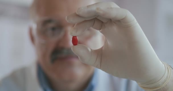 Чоловік-вчений тримає червону таблетку в руках і дивиться на неї крупним планом повільний рух — стокове відео