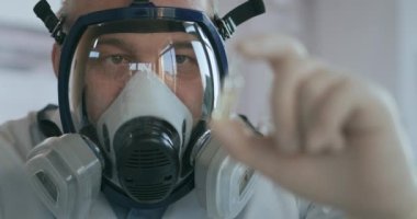 Bir ilaç şirketinde çalışan bir bilim adamı cam solunum cihazında laboratuarda ilaç geliştiriyor elinde virüse karşı aşısı olan beyaz bir tılsım tutuyor. 