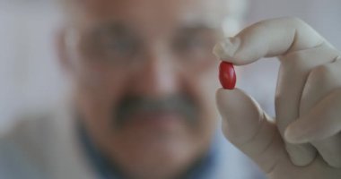 Bağışıklık, tedavi Covid-19 Coronavirus. Erkek bir bilim adamı elinde kırmızı bir hap tutuyor ve ona yavaş çekimde bakıyor.