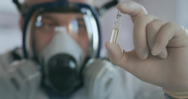 A scientist doctor at a pharmaceutical company developing a drug in a laboratory in a glass respirator screen holds a new medicine in his hands a white amulet with a vaccine against the virus — Stock Video