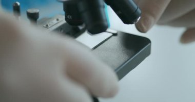 Mikroskop gözlüklerinin bir cam parçasındaki örneğe doğru çevrildiğini görüyoruz. Laboratuvarda metal mercekle yakın çekim örnek kaydırma ve mikroskop.