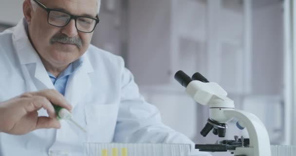 Cientista de Pesquisa Masculino. Ele sentado em um laboratório moderno high-end com Beakers, vidraria, microscópio e monitores de trabalho cercá-lo. — Vídeo de Stock