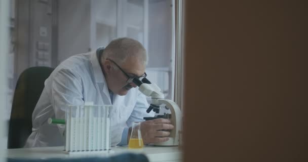 Cientista de Pesquisa Masculino. Ele sentado em um laboratório moderno high-end com Beakers, vidraria, microscópio e monitores de trabalho cercá-lo. — Vídeo de Stock