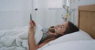 Evde yatarken cep telefonu tutan bir kadın..