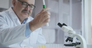 Laboratuvar. Mavi eldiven tüpleri hareket ettirir ve mavi sıvı damlatır. Test tüpünde sarı ve mavi sıvı numunesi tutan bir tıp çalışanı laboratuardaki idrarı analiz ediyor..