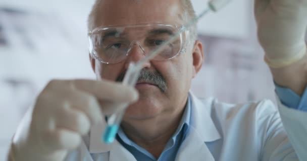 Techniker träufelt die Lösung vorsichtig aus der Pipette in Glasröhrchen für die DNA-Analyse. Arzt tropft blaue Lösung in Glasröhre, Coronavirus-Pandemie, Hände in Großaufnahme. — Stockvideo