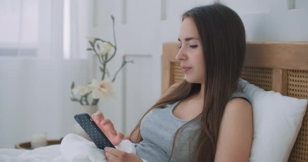 Frau hält Handy zu Hause im Bett. — Stockvideo