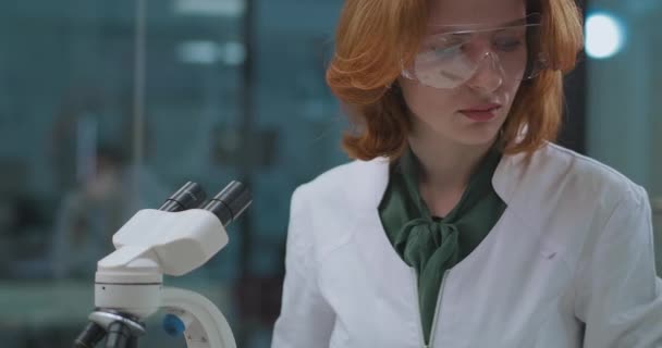 Портрет женщины лаборантки в клинике лечения ковид-19, специалист работает с микроскопом для исследования вируса — стоковое видео