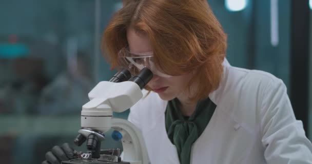 Donna biotecnologa sta lavorando in laboratorio di ricerca, visualizzazione del campione al microscopio, ritratto di persona esperta — Video Stock