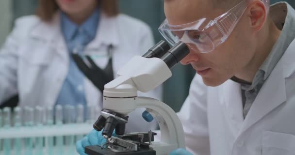 Microbiologista está pesquisando bactérias em laboratório, o homem está olhando por microscópio, pesquisa biológica — Vídeo de Stock