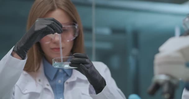 Pesquisas científicas em laboratório, homem e mulher estão trabalhando com reagentes químicos, visualizando reação por microscópio — Vídeo de Stock