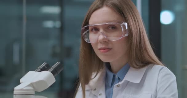 Kvinnlig expert på vetenskapligt laboratorium, arbetar med mikroskop, porträtt av ung kvinna i lab — Stockvideo