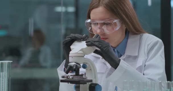 Медицинская работница изучает анализ в медицинской лаборатории, образцы ДНК и крови, исследуя в аппарате микроскопа — стоковое видео