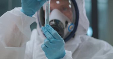 Kimyager laboratuvarda tehlikeli kimyasallarla çalışıyor. Bilim adamı koruyucu önlük ve maske giyiyor.
