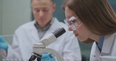 Adli tıp uzmanlarından oluşan bir ekip suç laboratuarında çalışıyor, kanıtları araştırıyor, kadınlar DNA örneklerini mikroskopla inceliyor.