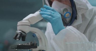 Tıbbi laboratuvarda biyolojik silahın geliştirilmesi, koruyucu önlüklü erkek bilim adamı bakteri ve virüsü mikroskopla inceliyor.