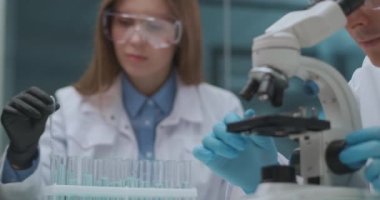 İki tıp uzmanı tıbbi klinik laboratuvarında testler yapıyor. Mikroskop ve reaksiyonlu test tüpleri üzerinde çalışıyorlar.