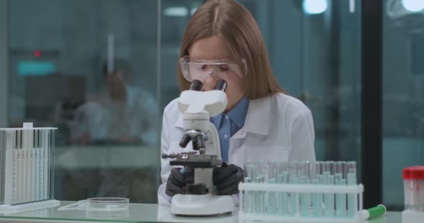 Microbioloog vrouw onderzoekt monster in laboratorium, op zoek naar microscoop, specialist van DNA-analyse, medisch lab — Stockvideo