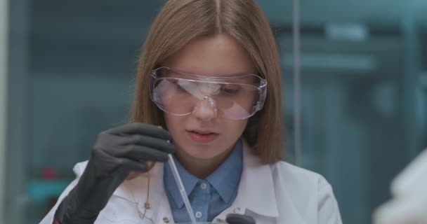 Student vid kemiska institutet gör praktiskt arbete i klassen, porträtt av ung kvinna med skyddsglasögon och vit klänning — Stockvideo