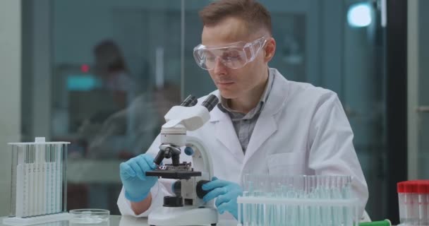 의학 연구소의 전문 기술자는 현미경 장비를 가지고 작업하고 있으며, 공들인 -19 를 위한 분석을 연구하고 있다. — 비디오