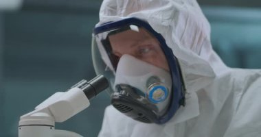 İnsan laboratuvarda bakteri ve virüsü araştırmak için modern elektronik mikroskop kullanıyor. Solunum cihazıyla kendini maskeyle koruyor.
