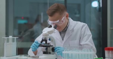 Virolog virüsleri laboratuvarda inceliyor, genç adam mikroskop kullanarak örnek alıyor, yüksek teknolojili yöntemler.