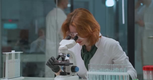 Эксперты в научной лаборатории, женщина-ученый исследует образцы в микроскопе, исследуя коронавирус — стоковое видео