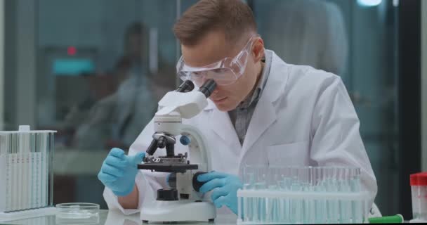 Genetische ingenieur onderzoekt de analyse in het laboratorium, kijkt in microscoop, experimenten met DNA — Stockvideo