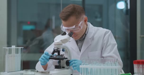 Ιολόγος μελετά ιούς στο εργαστήριο, νεαρός άνδρας χρησιμοποιεί μικροσκόπιο για την προβολή του δείγματος, υψηλής τεχνολογίας μεθόδους — Αρχείο Βίντεο