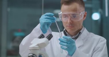 Laboratuvar asistanı analiz ve kimyasallar üzerinde çalışıyor. Test tüpünden alınan sıvıyı test tabağına yerleştiriyor.