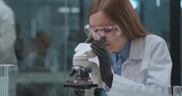 Médico fêmea está explorando a análise do paciente, usando microscópio em laboratório, DNA, sangue e engenharia genética pesquisa — Vídeo de Stock