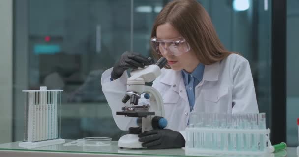 Junge Gesundheitsexpertin arbeitet im Labor und testet neuen Impfstoff von covid-19 mit modernem Mikroskop — Stockvideo