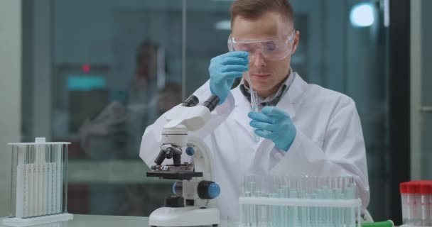 Giovane esperto chimico sta sperimentando in laboratorio, mescolando sostanza e liquidi in provetta, ricercando la reazione dei farmaci — Video Stock