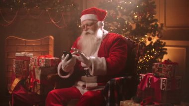 Noel Baba, Noel Gecesi 'nde evinde tek başına oturuyor ve akıllı telefon kullanıyor.