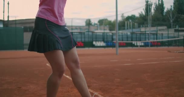 テニスをする女性の動きが遅い。スローモーション:テニスコートでボールを跳ねる女性のセクション。アスリートはテニスボールを提供します。若いです女性ありますヒットザボールとともに彼女のテニスラケットで日没 — ストック動画