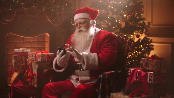 Santa Claus sedí sám ve své rezidenci na Štědrý večer a používá smartphone, přehrávání dotykovým displejem — Stock video